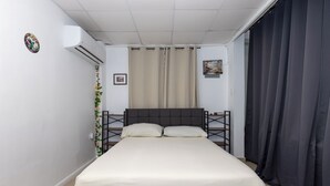 Ein Schlafzimmer mit einem Bett, Vorhängen, einer Klimaanlage und einem kleinen Bild an der Wand.