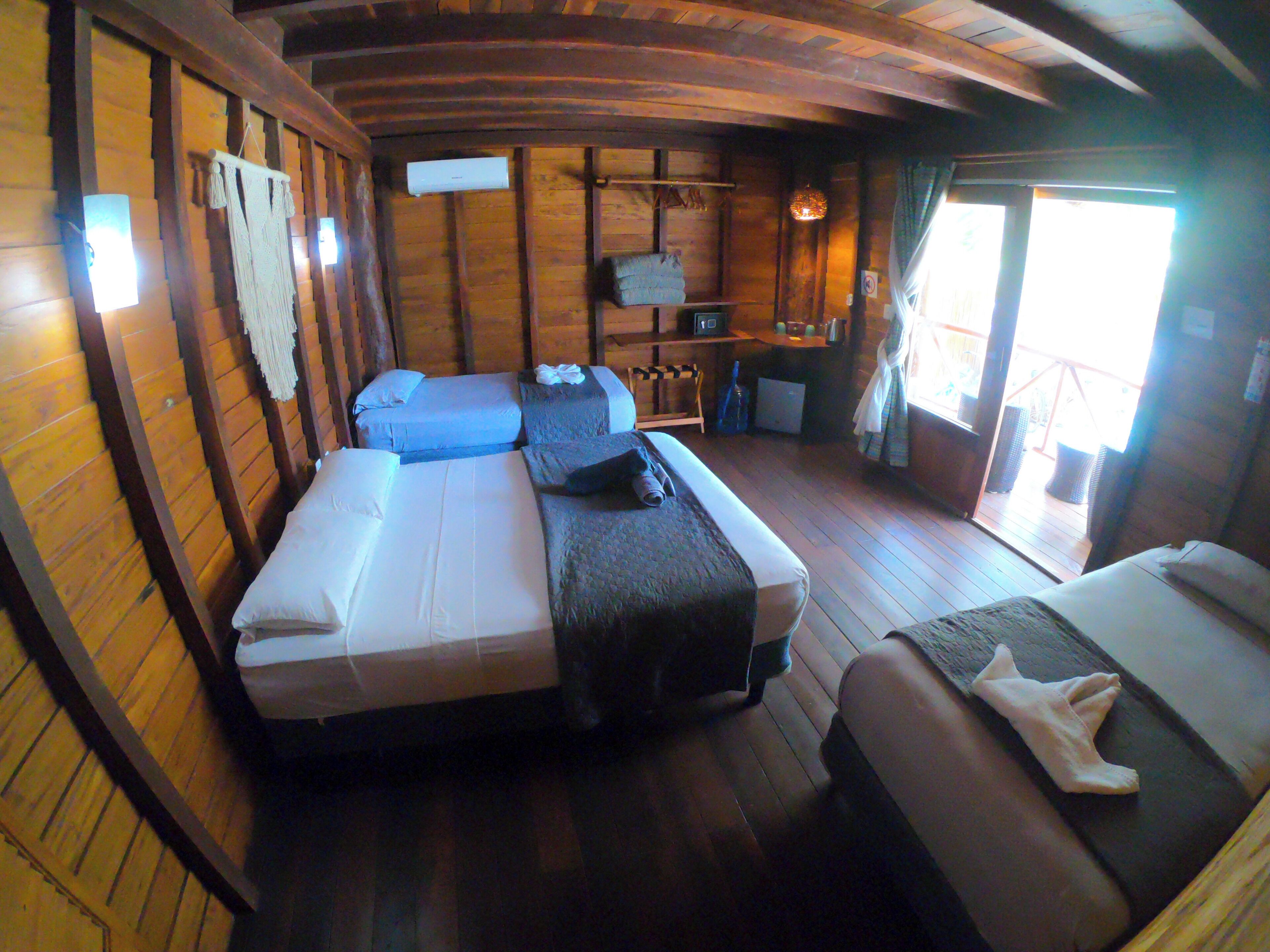 A cabin-style room with wooden walls and floors, two beds, a small desk, and a window.