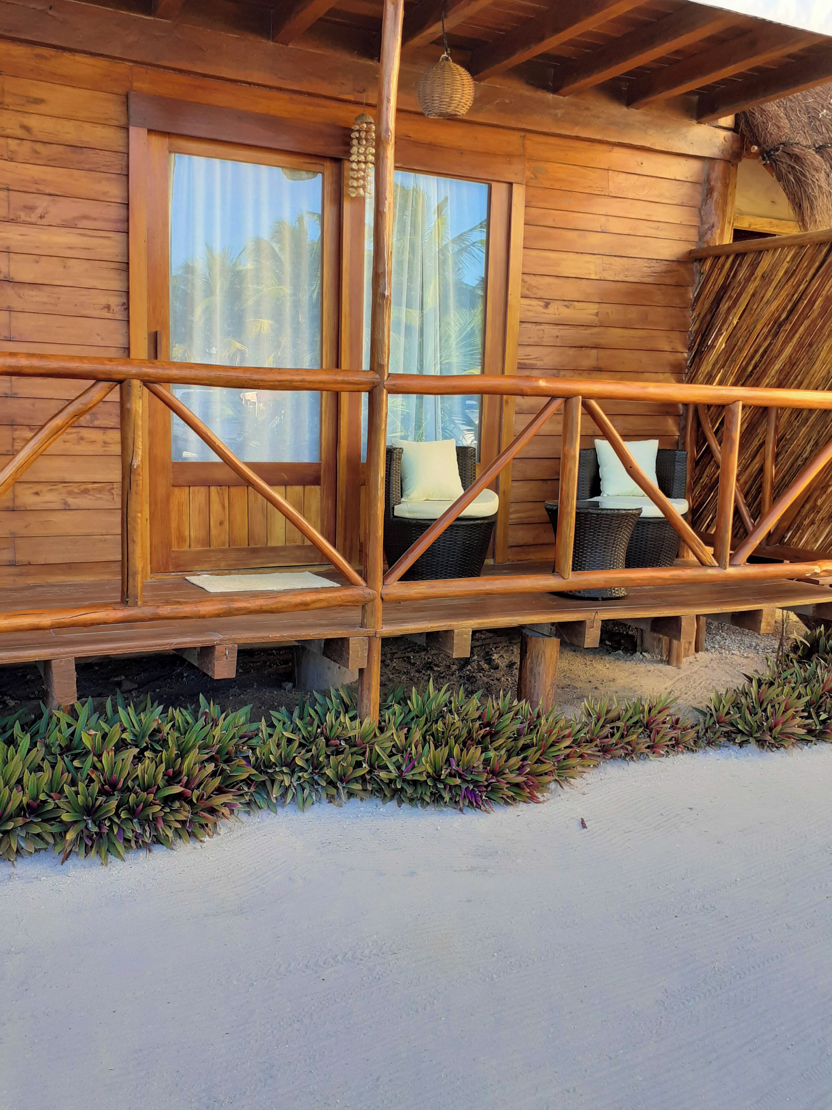 A wooden cabin with a porch, wicker furniture, and a thatched roof.