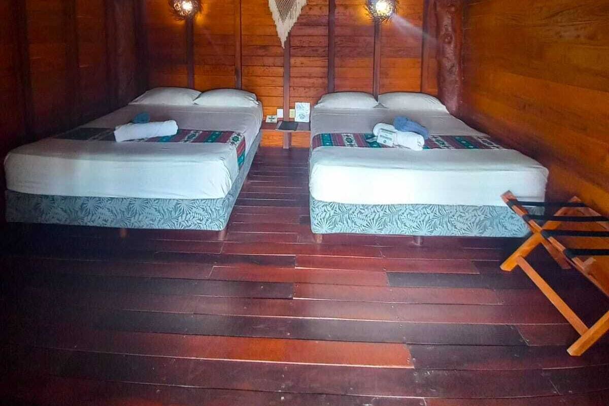 A room with two beds, wooden walls, a thatched roof, and a wall-mounted air conditioning unit.