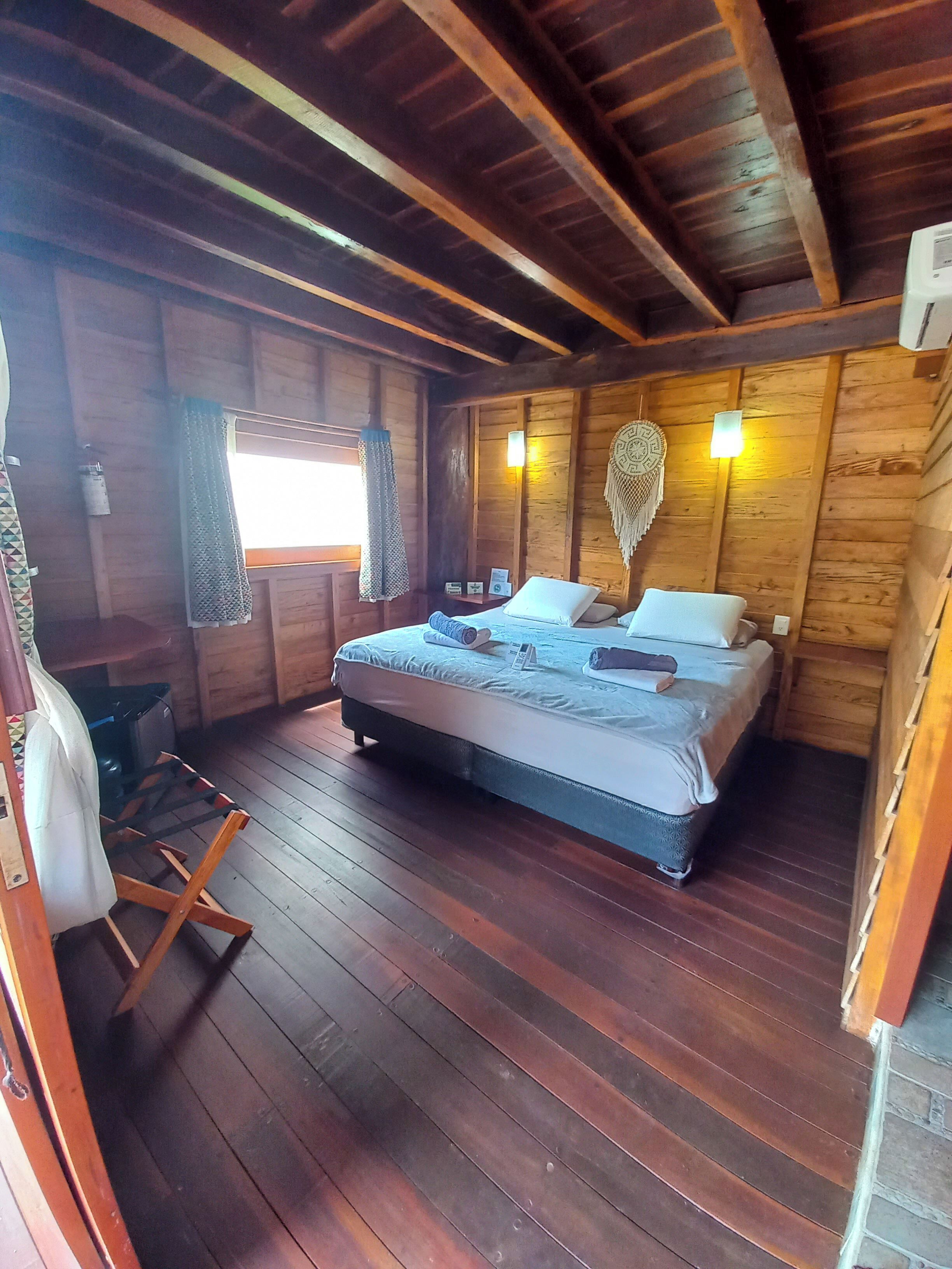 A wooden cabin bedroom with a bed, a small table, and a window with curtains.