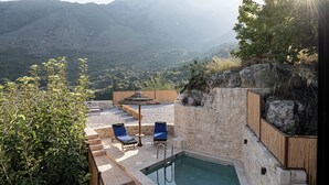 A pool area with lounge chairs and a stone wall, overlooking a mountainous landscape.