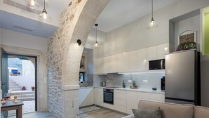 A modern kitchen with white cabinets, a stainless steel refrigerator, and a stone archway leading to a balcony.