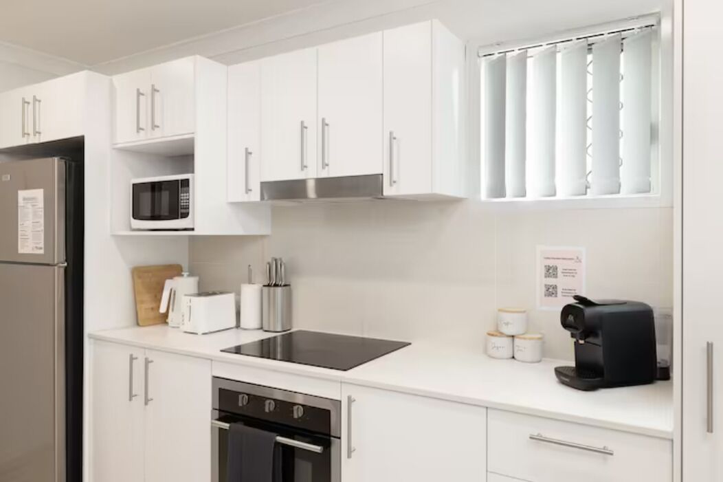 Una cocina moderna con armarios blancos, un refrigerador de acero inoxidable, un microondas, un tostador, una cafetera y un lavavajillas.