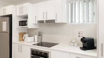 Una cocina moderna con armarios blancos, un refrigerador de acero inoxidable, un microondas, un tostador, una cafetera y un lavavajillas.
