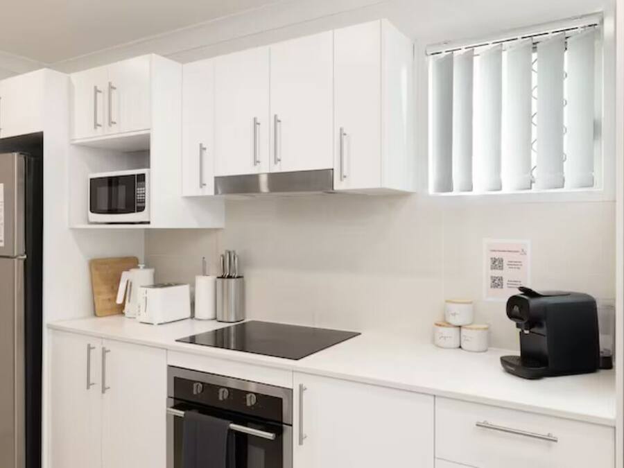 Una cocina moderna con armarios blancos, un refrigerador de acero inoxidable, un microondas, un tostador, una cafetera y un lavavajillas.