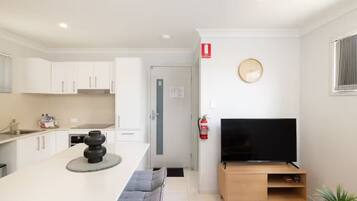 A modern kitchen with white cabinets, a central island with a black vase, and a flat-screen TV on a wooden stand.