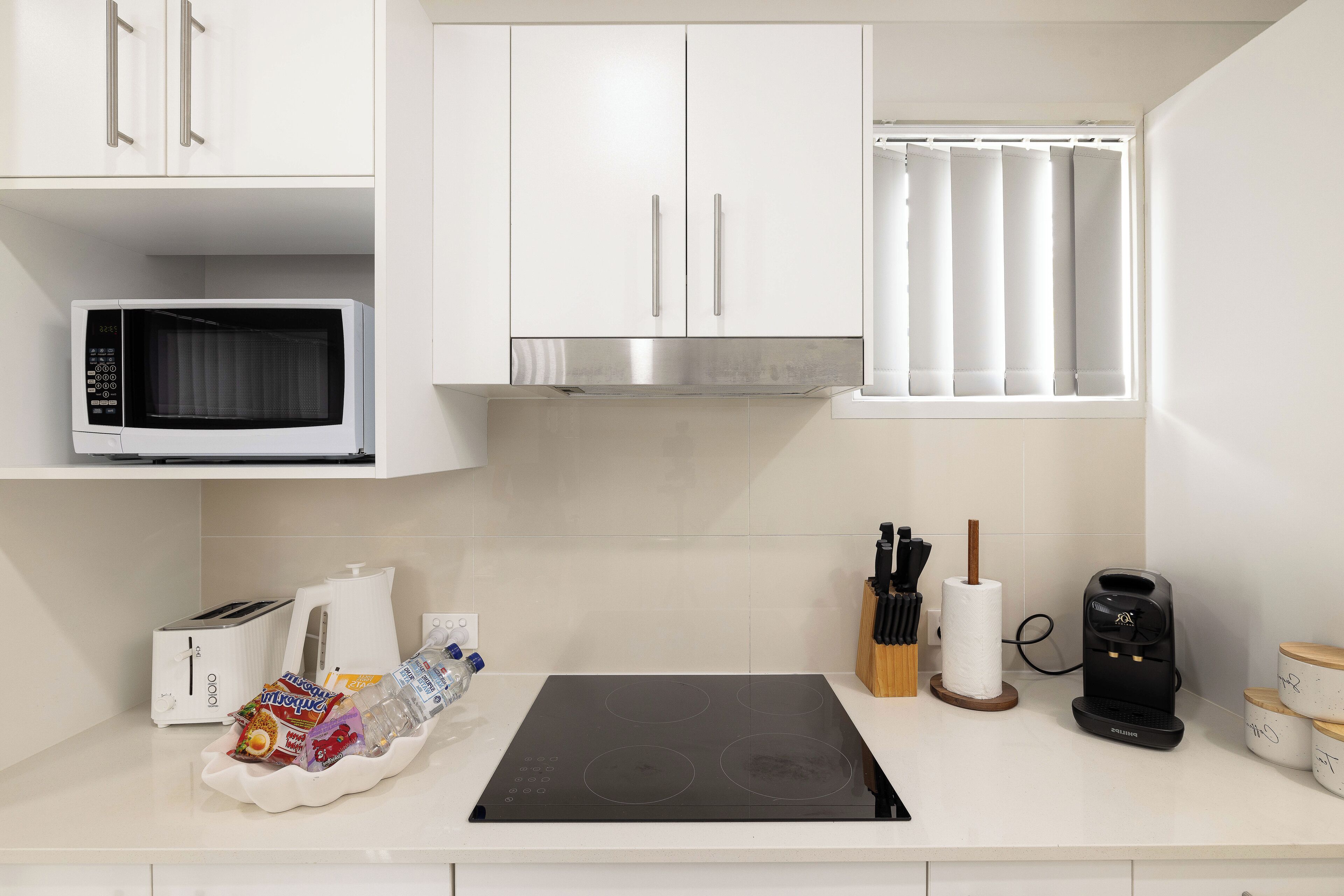 A modern kitchen with white cabinets, a microwave, a toaster, a kettle, and a coffee maker.