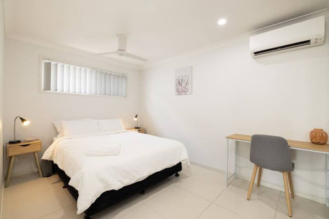 A bedroom with a bed, bedside tables, a desk, and an air conditioning unit.