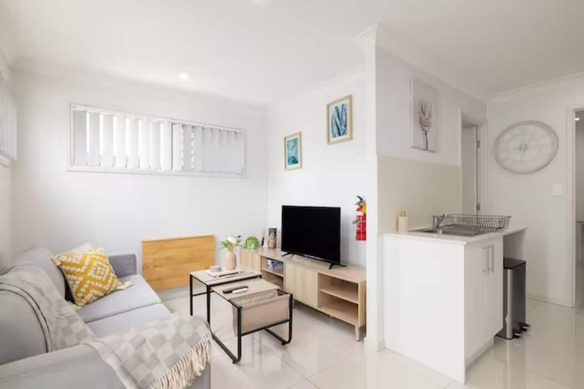 A modern living room with a sofa, TV, and a small kitchen area with a sink and cabinets.
