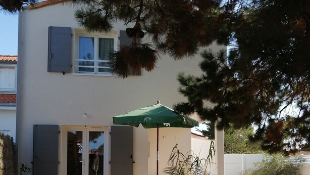 A patio with outdoor furniture, a green umbrella, and a building with a white exterior. - Charming new 70 m² house in the heart of the Pines (L'Aiguillon-la-Presqu'île)