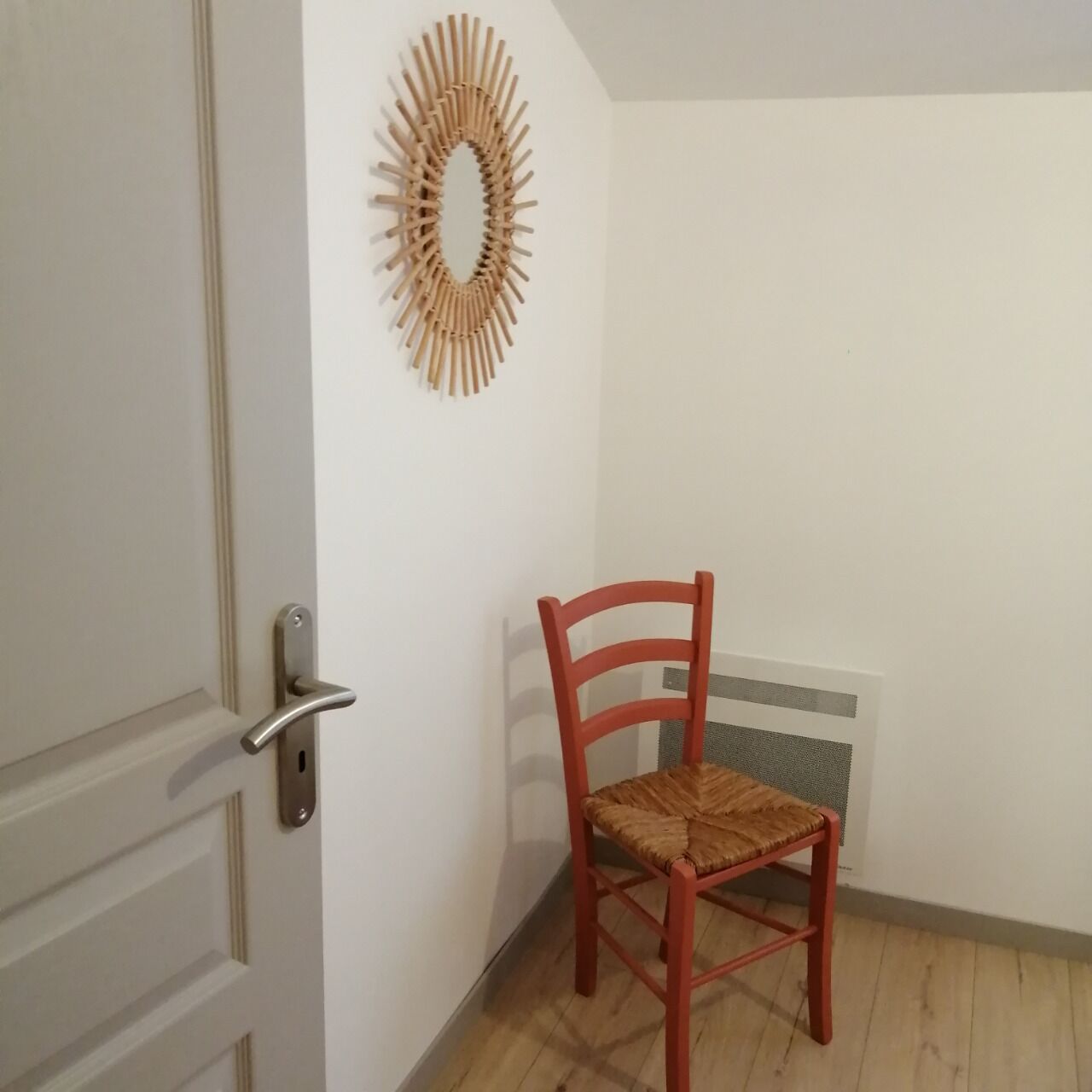 Een hoekzaal met een houten stoel, een radiator en een witte deur.