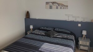 A bedroom with a bed, a nightstand, a lamp, and a wall art piece. - Charming new 70 m² house in the heart of the Pines (L'Aiguillon-la-Presqu'île)