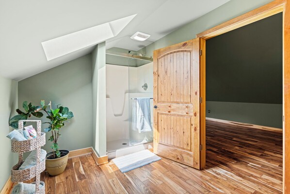 A room with a wooden floor, a potted plant, a glass shower enclosure, and a wooden door.