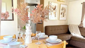 A dining area with a wooden table set for four, surrounded by cushioned chairs. - Harwich - Caravan - Sleeps 10 - Garden - Pool (Harwich)