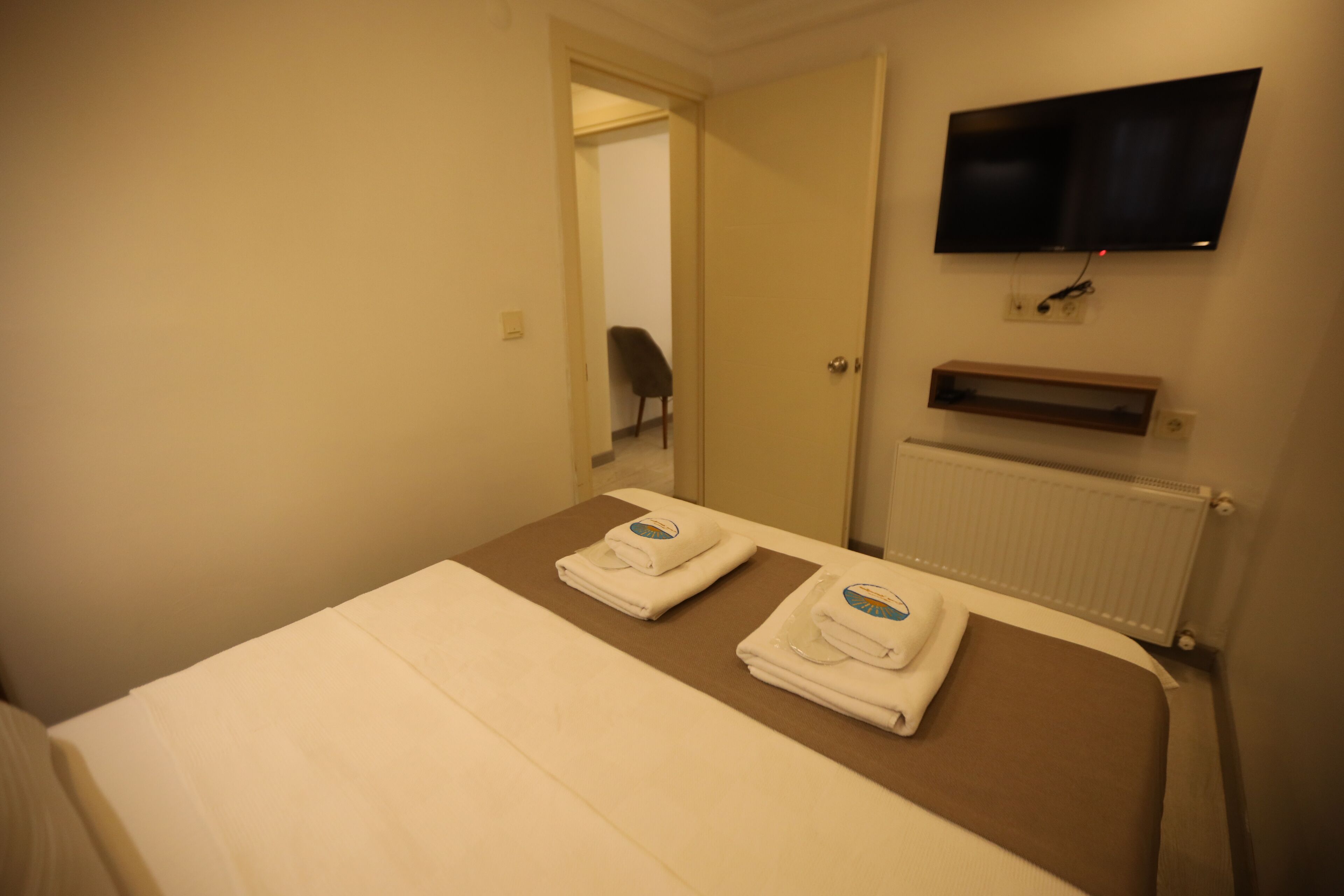 Une chambre d’hôtel avec un lit, un téléviseur fixé au mur et une petite étagère en dessous.