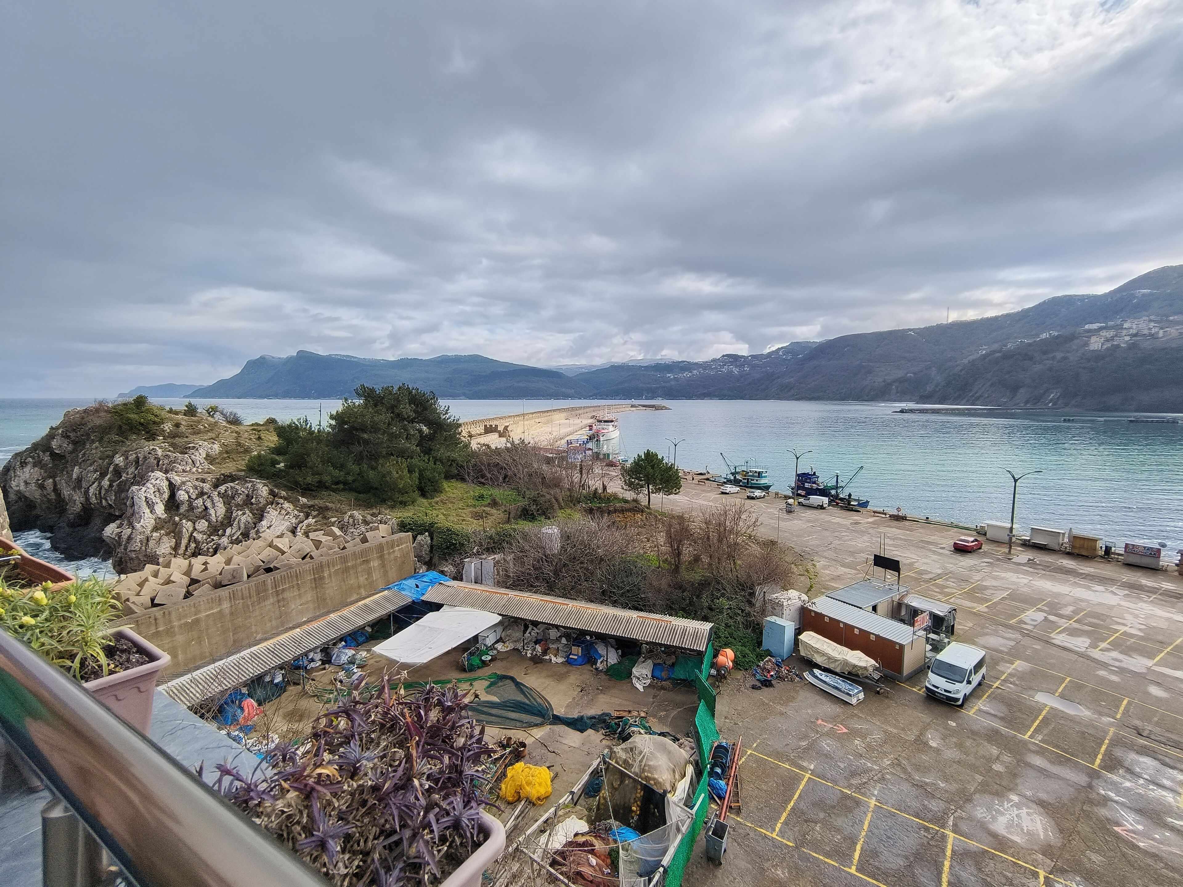 A coastal area with a rocky shoreline, a pier, and a parking lot with boats and vehicles.