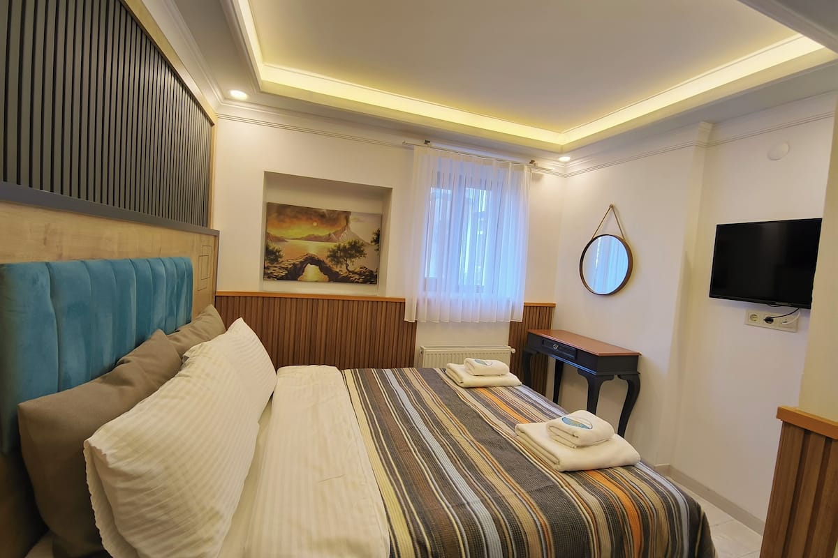 A hotel room with a bed, a painting, a television, and a desk.