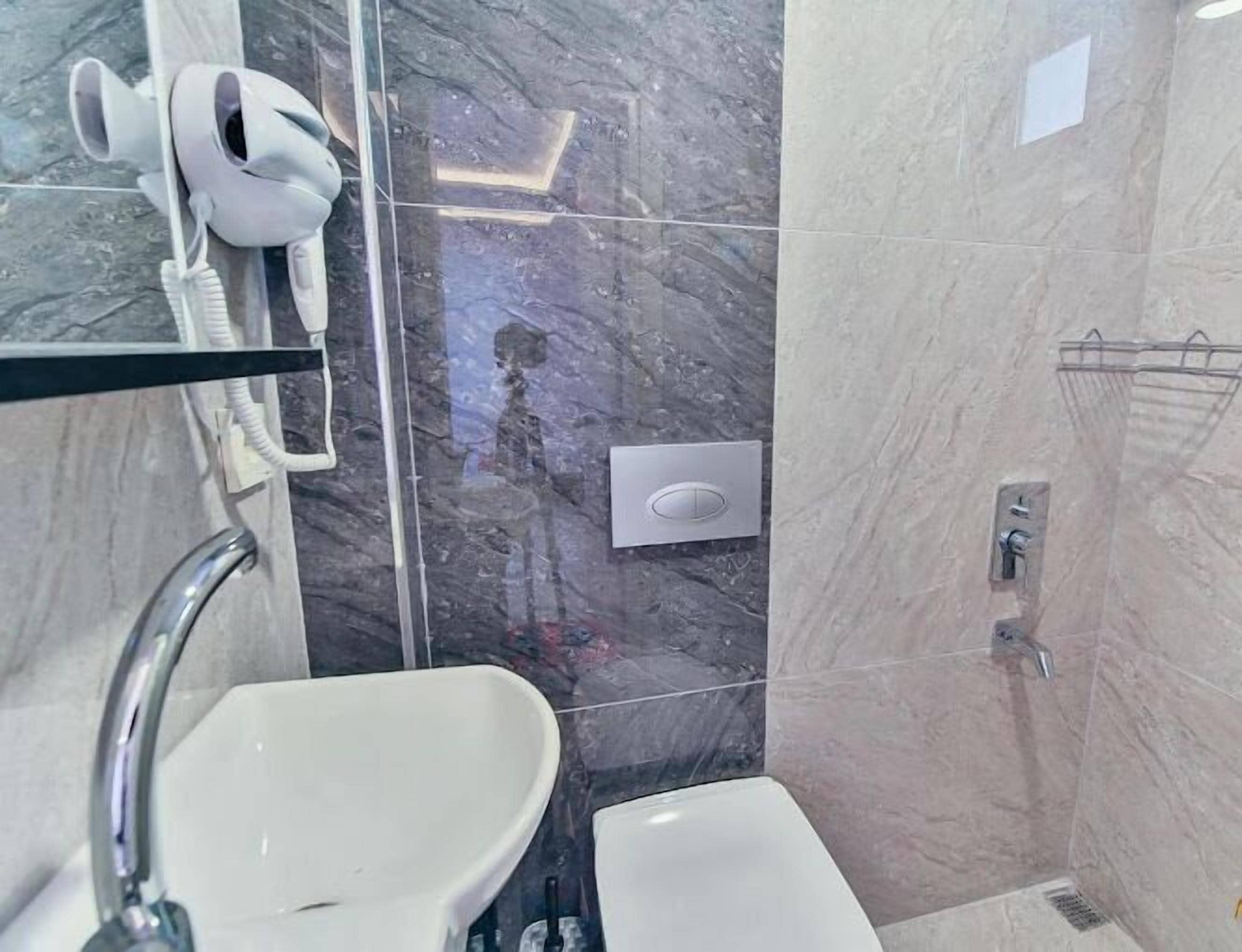 Casa de banho com lavatório branco, espelho, secador de cabelo e cabine de duche.