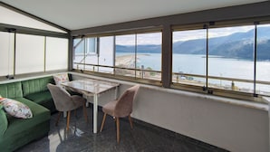 A room with a green sofa, two chairs, a table, and large windows offering a view of a lake and mountains. - AMASRA EMEK PANSİYON (Amasra)