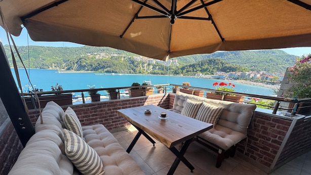 A patio with a cushioned sofa, a wooden table, and an umbrella. - AMASRA EMEK PANSİYON (Amasra)