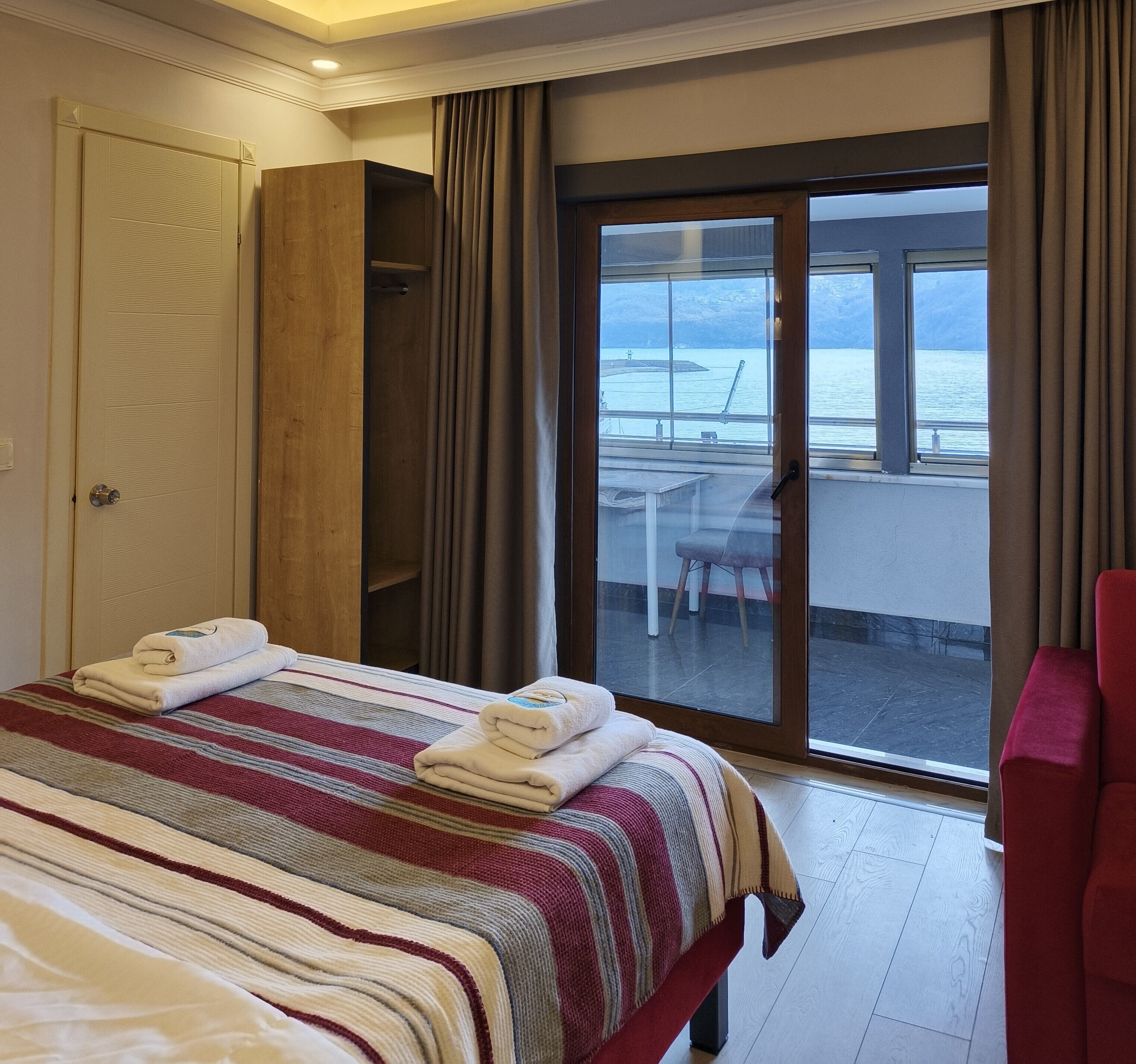 Ein Hotelzimmer mit Bett, einem roten Sessel, einem Balkon mit Tisch und Stuhl sowie Blick auf das Meer.