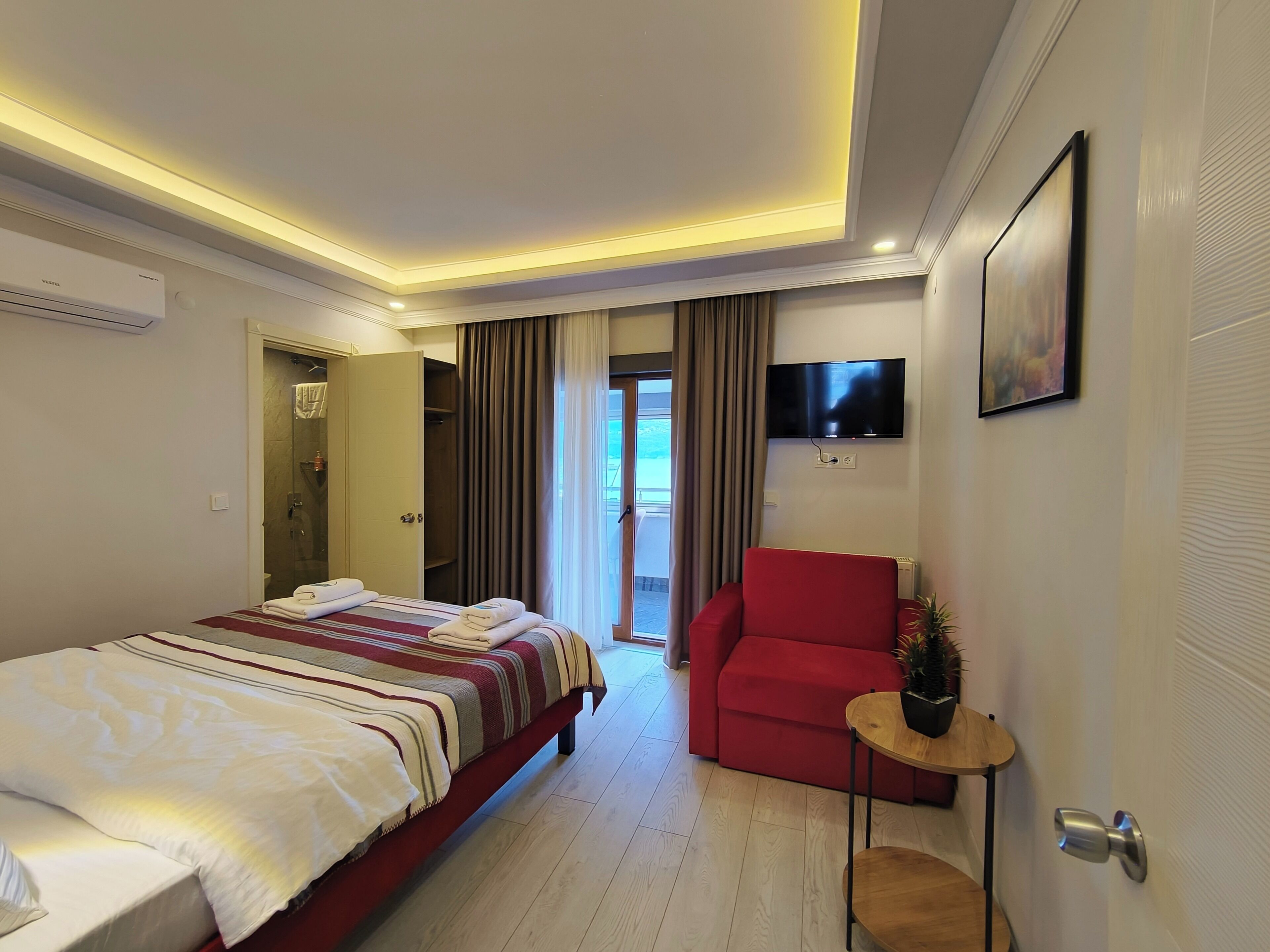 Habitación de hotel con cama, una silla roja, televisión y puerta al balcón.