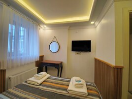 A hotel room with a bed, a desk, a mirror, and a TV.