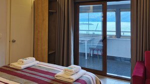 A hotel room with a bed, a wardrobe, a balcony with a table and chairs, and a view of the sea. - AMASRA EMEK PANSİYON (Amasra)