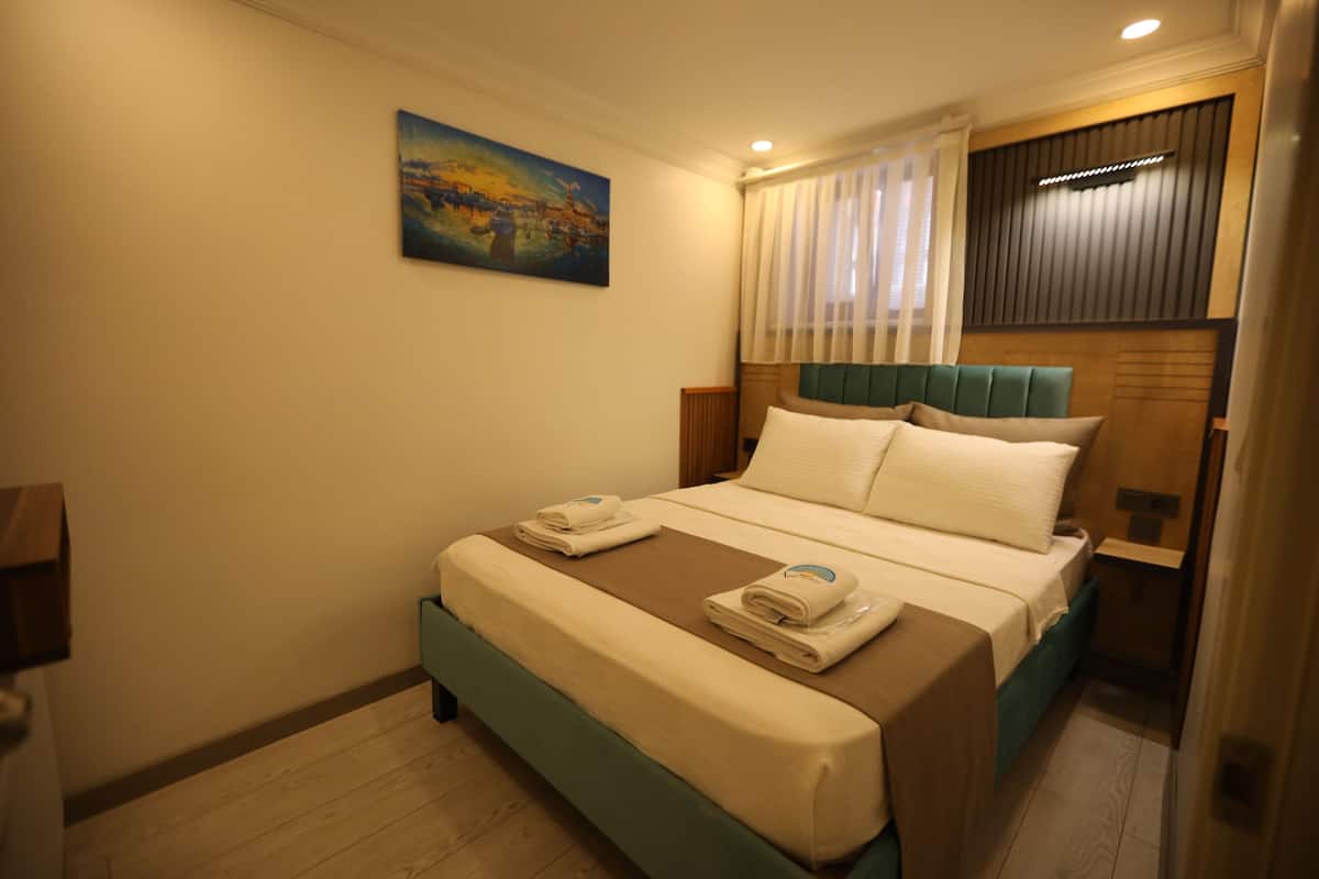 A hotel room with a bed, a painting on the wall, and a window with curtains.