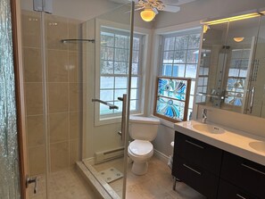 Een moderne badkamer met een douchecabine van glas, een toilet, een wastafel met spiegel en een raam met decoratief glas.