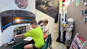 Ein spielbereich im Weltraum-Design mit einer Bedienkonsole, einem Raketenmodell und Astronautenfiguren.
