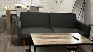 A modern living room with a gray sectional sofa, a wooden coffee table, and a dining area with a white table and chairs.