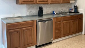 A kitchen with wooden cabinets, a stainless steel dishwasher, and a countertop with a coffee maker and utensils.