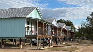 A row of wooden cabins with metal roofs, each with a balcony and a small porch area. - River View Double Queen Cottage near Downtown #24 (Kerrville)