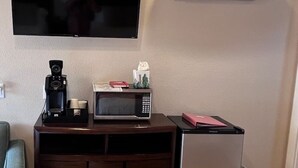 A compact living space with a flat-screen TV mounted on the wall, a coffee maker, a microwave, and a mini refrigerator.