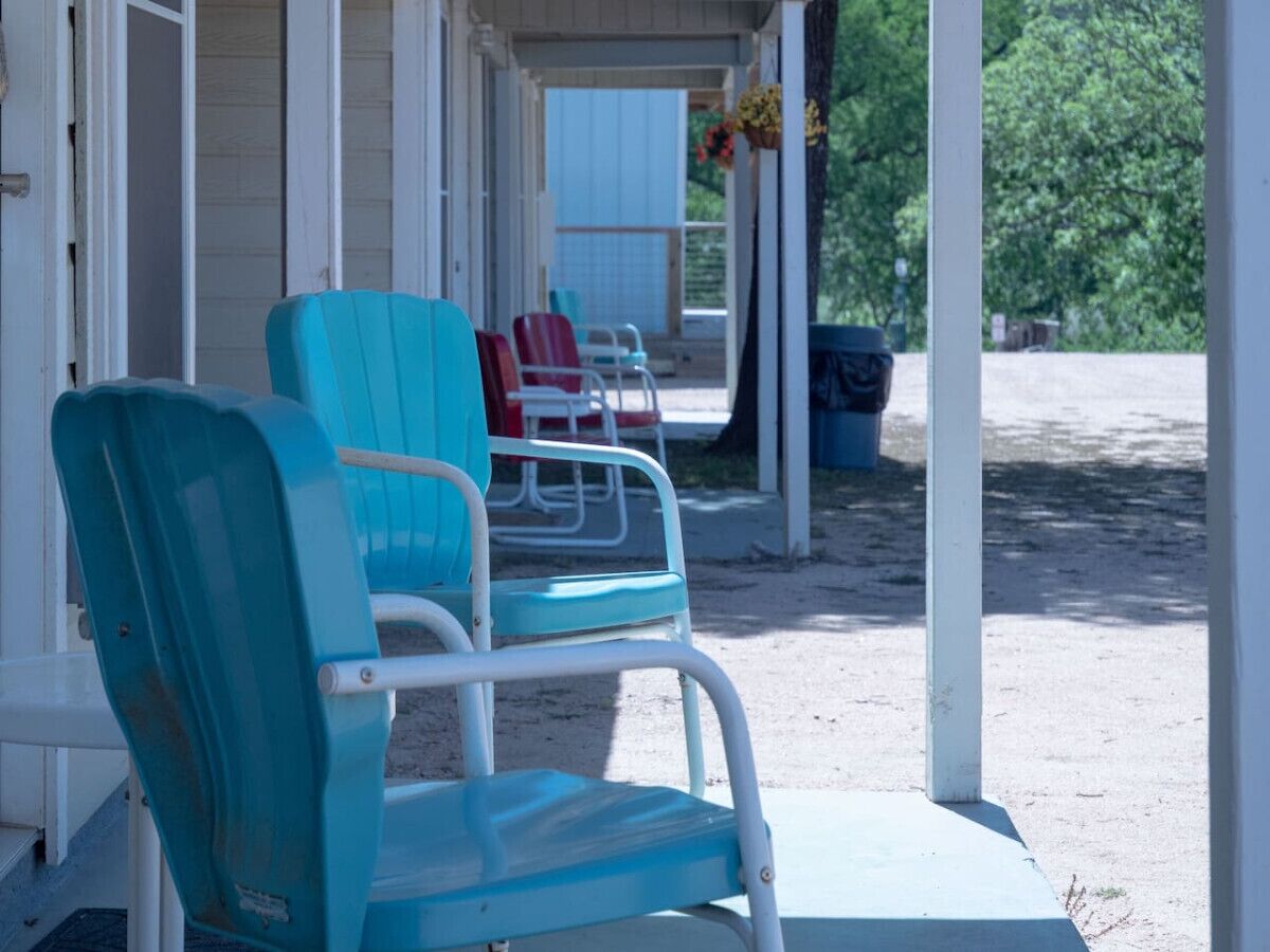 A covered porch with turquoise chairs and a red chair.