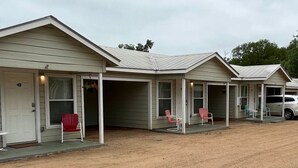 A row of single-story motel buildings with individual porches and front doors. - Single Level Double Queen Beds Cabin 2 w/ Carport (Kerrville)