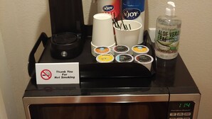 Un microondas con cafetera, un recipiente de la marca Njoy, una botella de gel antibacterial de aloe vera y un cartel agradeciendo a los huéspedes por no fumar.