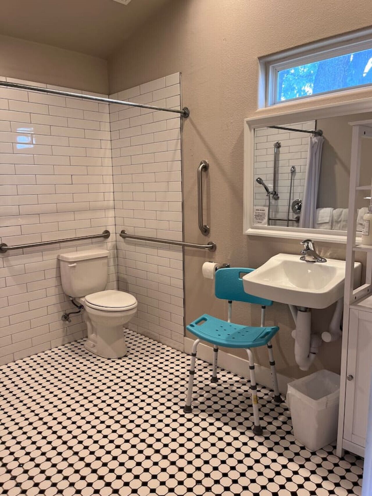 A bathroom with white subway tiles, a toilet, a sink, a shower, and a blue chair.