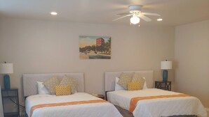 A hotel room with two beds, a ceiling fan, and a painting on the wall.