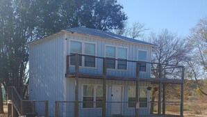 A two-story building with a balcony on the upper floor, a front porch, and a fenced area.