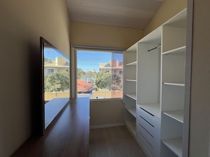 A narrow room with a large window, wooden floor, and white built-in shelving.