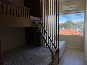 Een kamer met een stapelbed, een raam met uitzicht op gebouwen en bomen, en een luchtverkoeler aan het plafond.