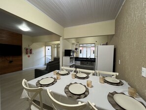 Un coin repas avec une table dressée pour quatre personnes, une cuisine en arrière-plan et un téléviseur fixé au mur.