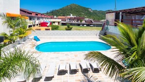Piscina con sillones de descanso, rodeada de palmeras y vista a una ladera.