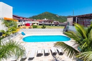 Une piscine entourée de chaises longues, de palmiers et offrant une vue sur une colline.