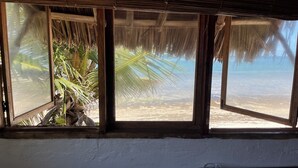 Een kamer met uitzicht op het strand, een rieten dak en een palmboom ervoor.