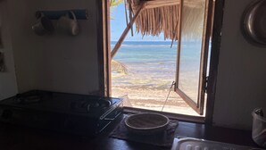 Een keuken met een fornuis, een spoelbak en uitzicht op het strand door een open deur.