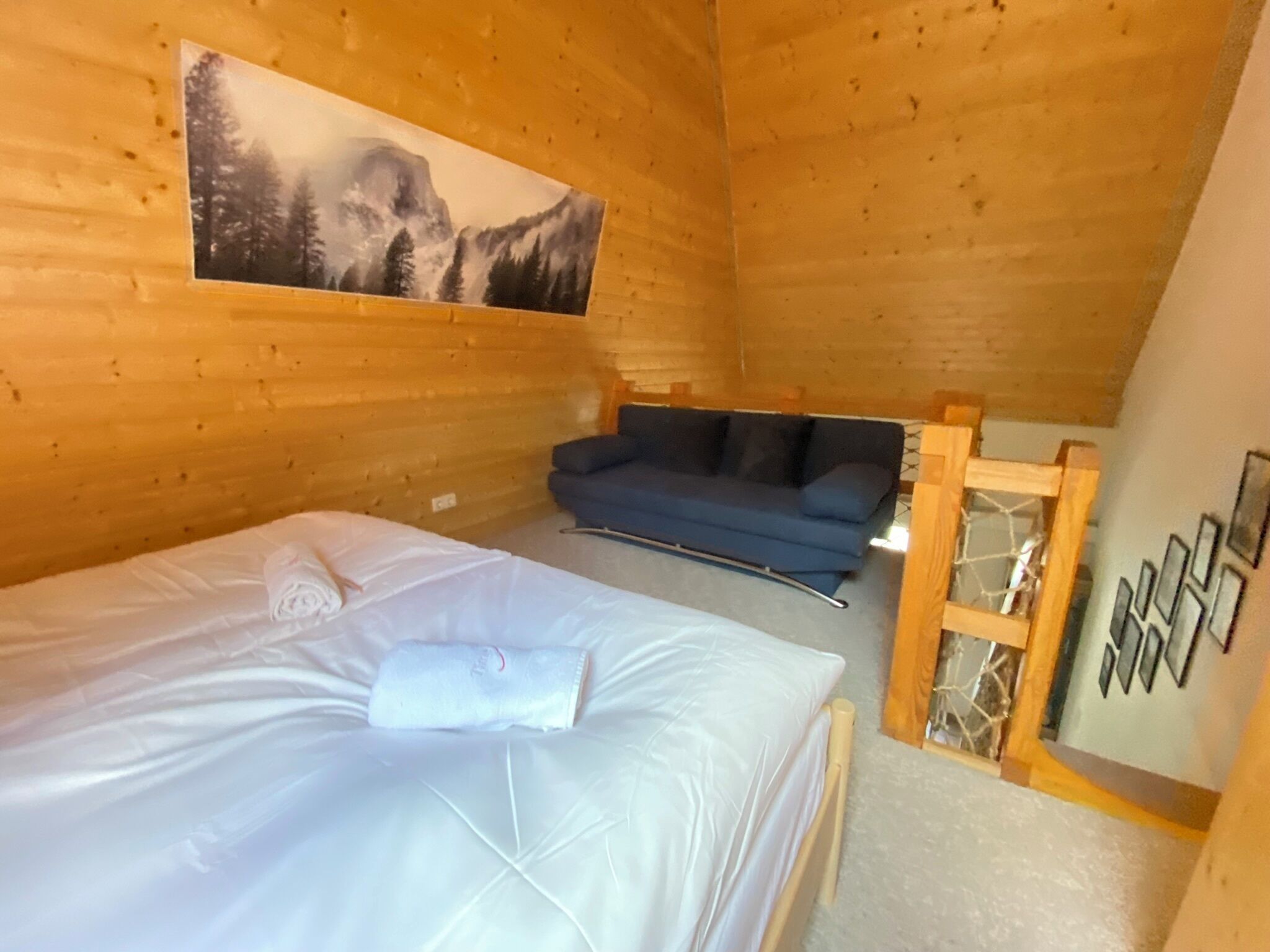 Ein gemütliches Holzhütten-Zimmer mit einem Bett, einer blauen Couch und einem Gemälde einer Berglandschaft.